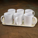 Six plain white ceramic mugs arranged in two rows rest on a Dairy Cattle themed melamine serving tray by Alex Underdown from Countryside Greetings, with a light base, displayed against a brown surface.
