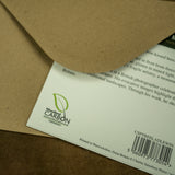 A close-up of Countryside Greetings Frost Kissed Beech Trees A5 woodland card, partially in a brown envelope. Features the Woodland Carbon logo, barcode, and info on its eco-friendly UK production certified by the Woodland Carbon Code.