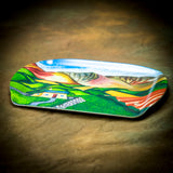The A Safe Haven, Brecon Beacons melamine serving tray by Amanda Skipsey from Countryside Greetings features a vibrant Welsh landscape with green fields, a white cottage, winding paths, and hills beneath a blue and orange sky.