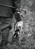 A black and white image of a person in outdoor gear holding a duck and walking stick in tall grass features on the 10 Shooting notecards with envelopes by Charles Sainsbury-Plaice from Countryside Greetings.