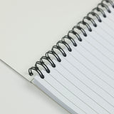 Close-up of the Countryside Greetings Cartoon dog themed A6 lined notebook, Innocent by Bryn Parry. Features lined white pages, visible spiral binding, and a playful dog cartoon peeking from the corner against a plain background.