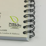 Close-up of the Bird themed A6 lined notebook, Woodpecker by Dick Twinney from Countryside Greetings, showing a Woodland Carbon logo and website on the cover. This A6 lined notebook features a plain white background.