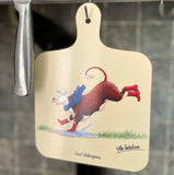 The Beef Wellingtons cow themed mini chopping board by CountrysideGreetings hangs on a hook, showcasing Alex Underdown’s cartoon cow in red boots and blue scarf splashing in a puddle, with Beef Wellingtons and the artist’s signature below.