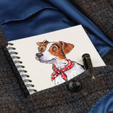 The Cartoon dog themed A6 lined notebook Jack Russell by Bryn Parry from Countryside Greetings, featuring a cute brown and white dog in a red scarf, peeks from a blue tweed coat pocket—an ideal gift for dog lovers.