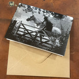 The Horse Riding and Hunting Greeting Card: Gate Closing by Charles Sainsbury-Plaice from Countryside Greetings features a black-and-white photo of a rider near a wooden gate, displayed on a brown envelope on wood.