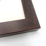 Close-up of a dark brown wooden frame corner, highlighting the rich grain and a white background, with Countryside Greetings Spaniel cocker spaniel dog cartoon signed print—The Kennel Dog by Bryn Parry just peeking through.