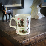 A white ceramic mug with bryn parry cartoon characters and text, sitting on a rustic wooden table with a black horse figurine and a white ceramic bird figurine in the background.